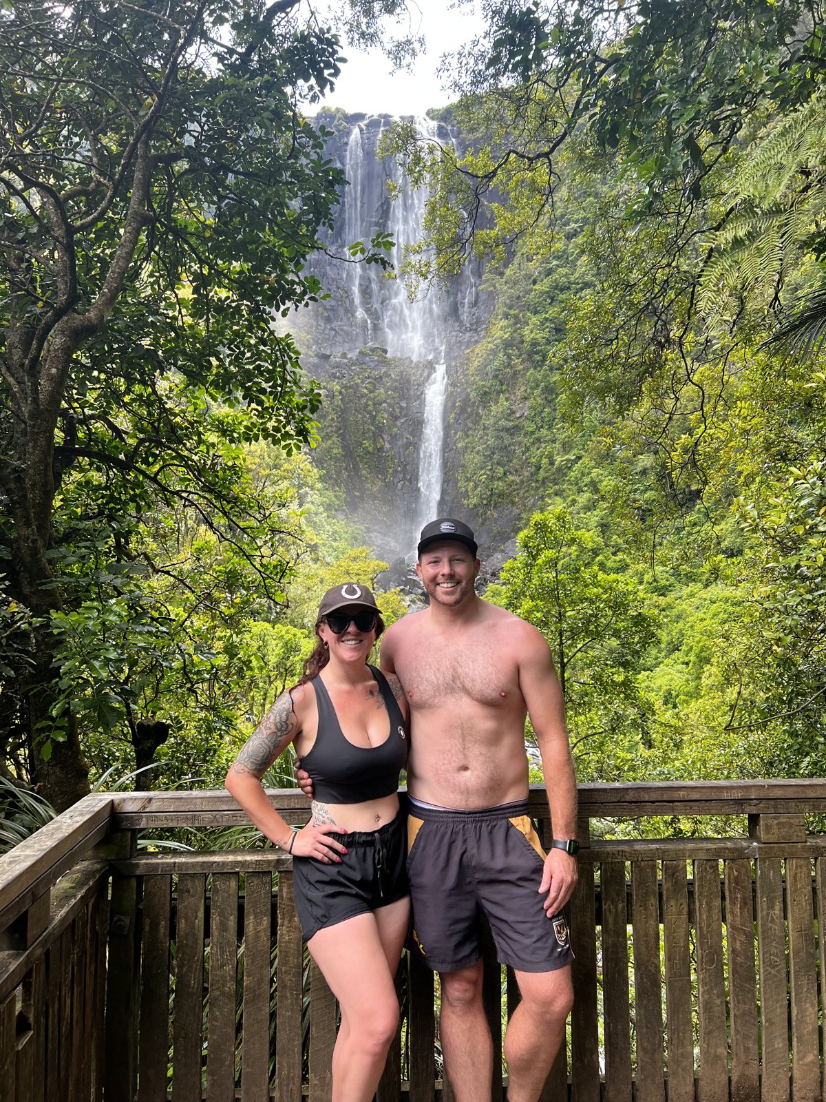 Dani and Alex in front of a tall rainforest waterfall