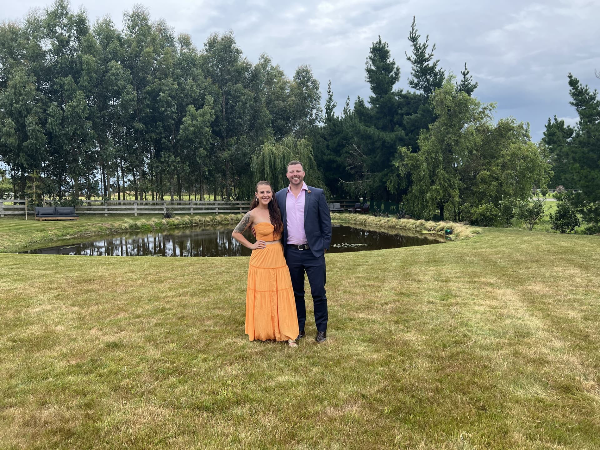 Alex and Dani standing together in a paddock beside a pond