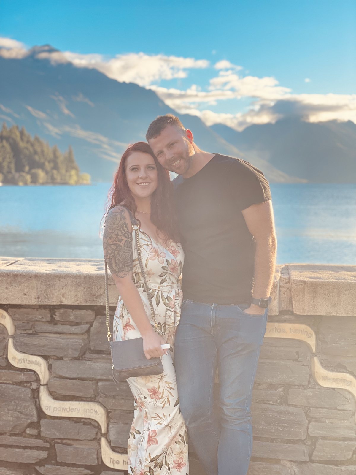 Dani and Alex on a stone wall above a lake and mountains