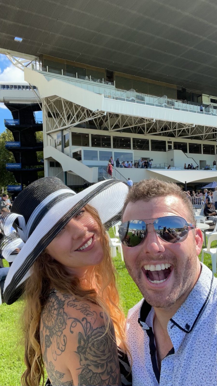 Dani in a wide-brimmed hat with Alex at the races
