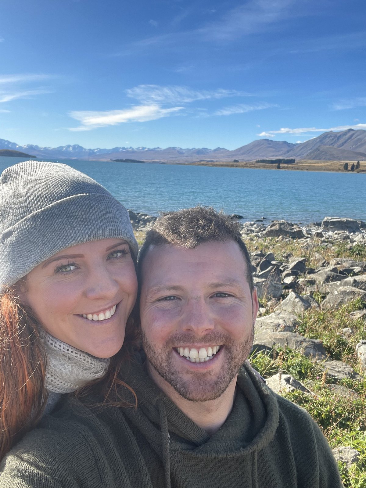 Dani and Alex bundled up beside a blue alpine lake